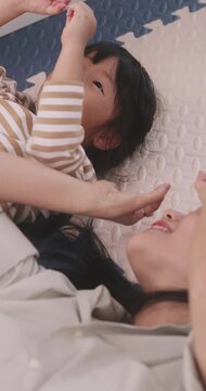 Cute Asian girl and her mother lying down on the floor playing and laughing together.