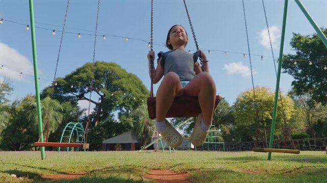A young girl enjoys swinging on a sunny day, surrounded by a vibrant playground. Ideal for family-oriented content and childhood nostalgia themes.