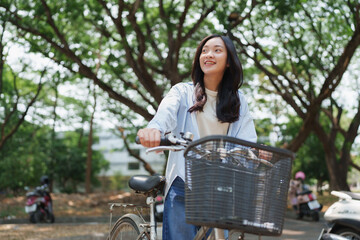 Young woman smiling walking bicycle on campus path © Phimwilai
