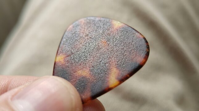 Close up of a guitar pick featuring speckled pattern and varying tones