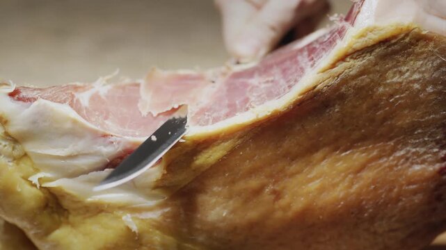Slow motion closeup of professional chef slicing dry cured serrano ham with sharp knife.