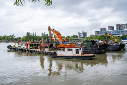 A fleet of industrial dredging barges equipped with  excavators and heavy machinery sits moored along riverin Ningbo, China. Concept of waterway maintenance and industrial activity 