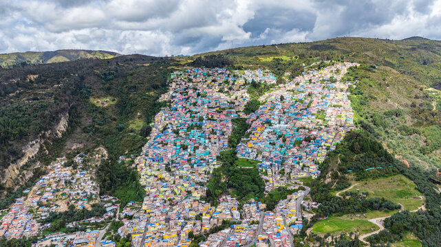 A vibrant hillside community in Bogot&aacute; with multicolored houses, showcasing urban transformation under a cloudy sky.