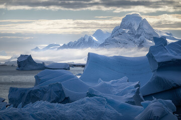 Large icebergs drift beneath snow-covered mountains in Antarctica. © Tom