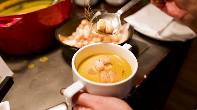 Adding Toasted Croutons to a White Mug of Creamy Pumpkin Soup