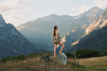 Fototapeta premium Cheerful woman outdoors, standing on a rock with distant mountains, sunny day, casual outfit, sense of adventure, natural colors, open landscape, relaxed lifestyle
