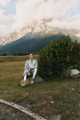 Fototapeta premium One person sits on a rock in a meadow, gazing thoughtfully at distant mountains, wrapped in a cozy cardigan for a quiet outdoor moment