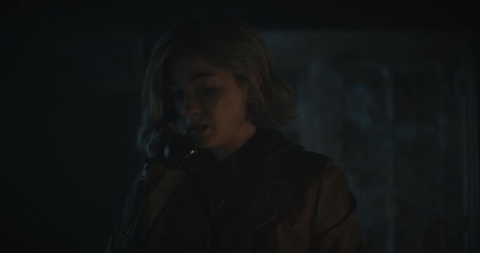 Lightning flashing outside as nervous young woman in dark room talks on rotary phone - closeup shot