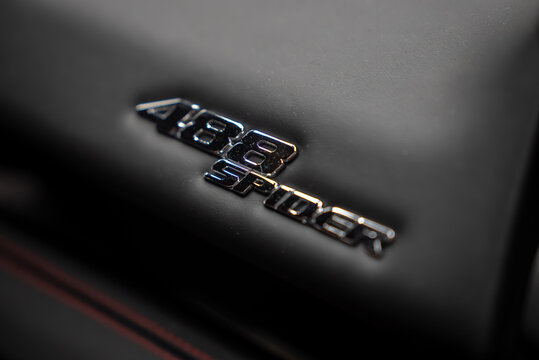 A tight close up shows the 488 Spider chrome badge set in black leather with red stitching, shallow depth of field, moody indoor light, and a focus on branding.