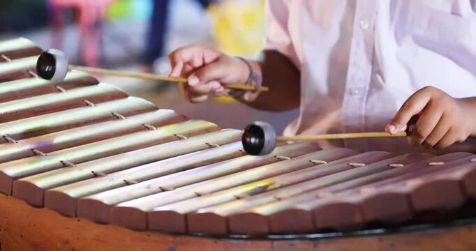 Hands playing a wooden xylophone with mallets, Thai school students perform xylophone outdoors at night market, Showcasing traditional music culture, close-up