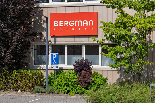 Amsterdam, Netherlands - 23 May 2026 - The exterior facade of Bergman Clinics in Amsterdam, showing the red company sign, windows, and a handicapped parking sign surrounded by green plants.