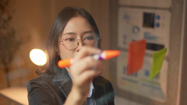 Asian businesswoman writing on a glass board at night