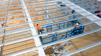 Steel structure construction: Workers in a lift platform work on the metal frame of a building, symbolizing industrial progress and development. © Rassarin