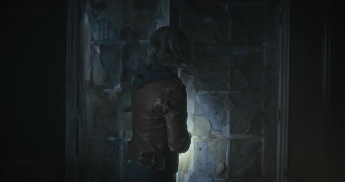 Silhouette of young woman with flashlight cautiously entering scary room and props door open then opens small chest as as storm rages outside 