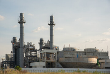 Obraz premium Power Plant Infrastructure: A contemporary power generation facility stands under a clear sky, showcasing its industrial complex of turbines, cooling towers, and exhaust stacks.