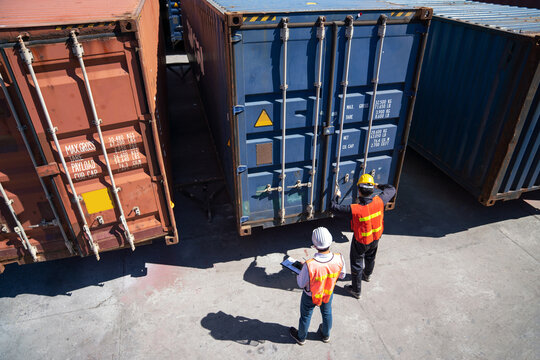 Shipping Containers at Port: Two workers in high-visibility vests oversee the loading and unloading of large shipping containers at a busy port, symbolizing global trade and logistics.