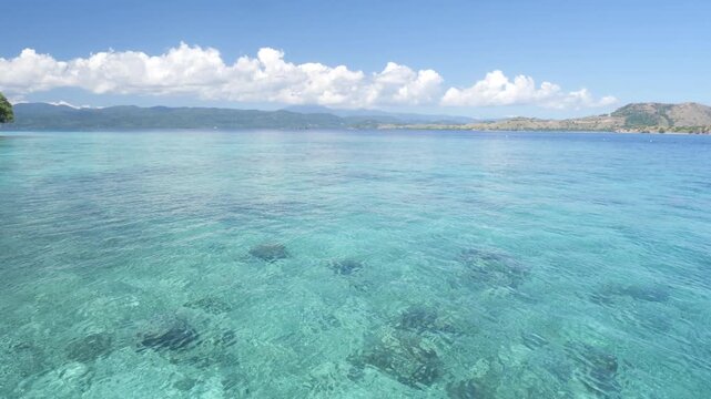 Side view from boat cruising across the blue waters near Komodo National Park, Hatamin island, Indonesia, with tropical islands, calm sea, and clear sunny sky