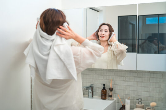 A woman towel-dries her hair in the bathroom after taking a bath.