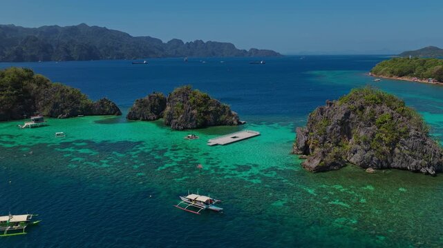 Drone orbit right shot around a white boat anchored on a crystal clear shallow coral reef flat in Coron, Palawan.