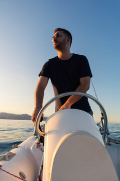 Young man steering a boat at sunset