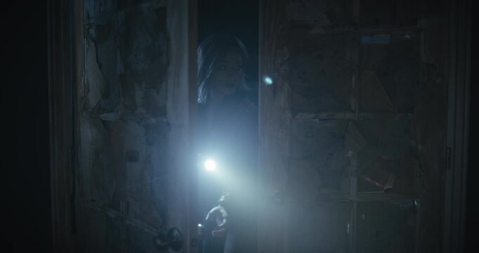 Cautious woman with flashlight entering spooky room and propping door open behind her - medium shot