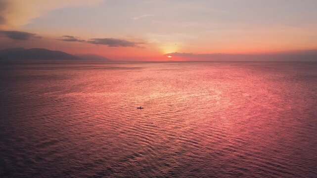 Wide aerial sunrise over tropical ocean with tiny fishing boat