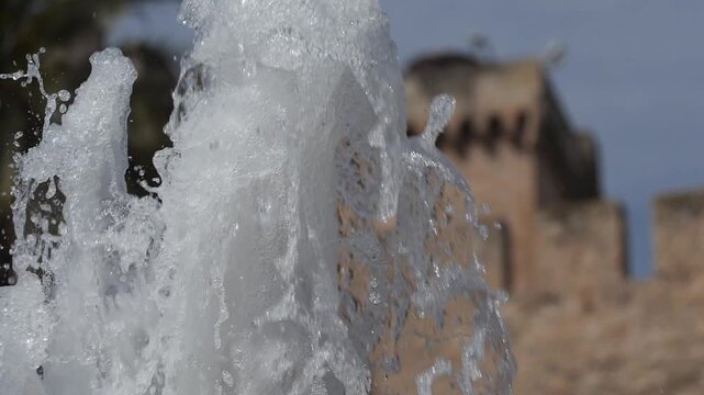 Super slow motion of a fountain jet with the blurred medieval walls of the Altamira palace in the background. Elche, Spain.