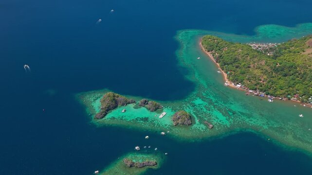 Aerial forward tracking shot over a bright turquoise coral reef edge drop-off into deep blue ocean in Coron.