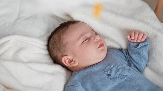 Newborn boy sleeping in a blue sweater with raised hand on a soft white blanket in a nursery cradle, eyes closed and relaxed; quiet serenity.