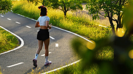 Fototapeta premium Active young woman jogging on a scenic park path during beautiful golden hour sunset for health and fitness concept