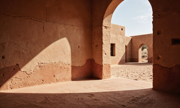 Adobe arch shadow defines a rustic terracotta interior with sunlight streaming across earthen walls and copy space for design