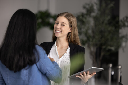 Two young businesswomen, workmates greeting each other in workplace with handshake gesture, express friendly relations, mutual respect. HR manager and female applicant shaking hands in company office