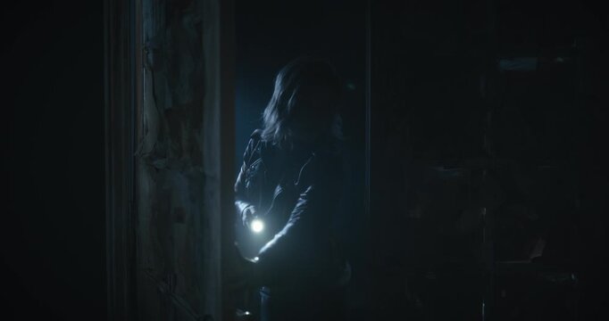 Nervous, cautious woman with flashlight entering dark, spooky room and propping door open with book behind her