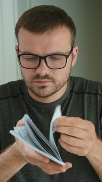 Man wearing glasses flipping through an instruction manual, showing product information, user guide, documentation, learning, setup, and careful reading.