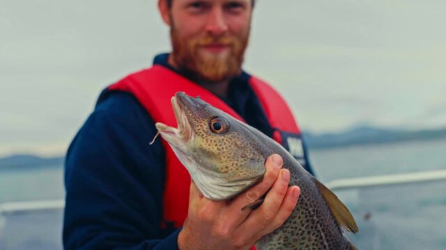 A Caucasian Fisherman In A Boat Holding A Freshly Caught Cod Fish. Close-up Shot