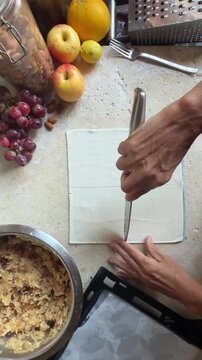 woman hands preparing food in kitchen, making apple strudel cakes with puff pastry and fresh ingredients