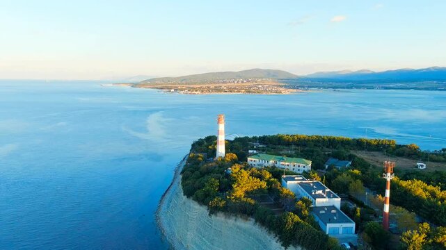 Gelendzhik, Russia. The octagonal Gelendzhik Range Lighthouse on Cape Tolstoy, its white tower with red horizontal bands rising above dense green canopy, Drone footage over calm Black Sea waters at d