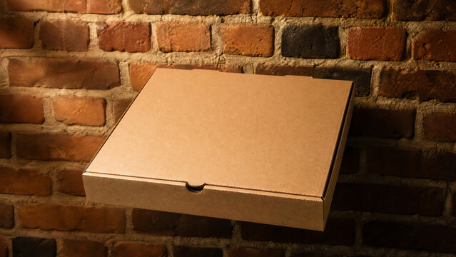 A simple cardboard box placed against a rustic brick wall, perfect for packaging pizza or takeout meals.