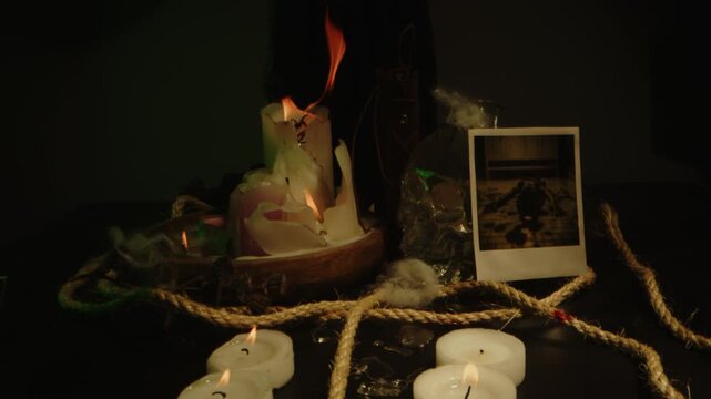Eerie dolly in of an occult altar with burning candles, a glass skull and an old book with bloody ropes and a polaroid picture