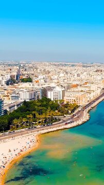 Vertical video. Bari, Italy. The central Lungomare embankment, Drone footage over the Adriatic with stone breakwaters, sandy beach, and dense white cityscape under clear summer skies. Drone footage, 