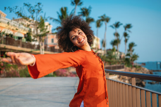 Beautiful woman joyfully raises her arms high celebrating life against a vibrant tropical background