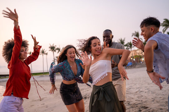 Energetic friends celebrating a summer party on the beach at sunset, embodying the carefree vacation