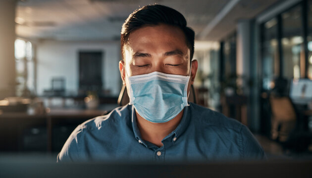 Man wearing face mask sneezing while working on computer in office