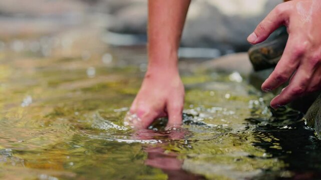 A man refreshes and rinses his hands in the cool water of a mountain stream, video in slow motion. Hands splash clear water in a shallow stream, The theme of tourism is mountain hiking and outdoor