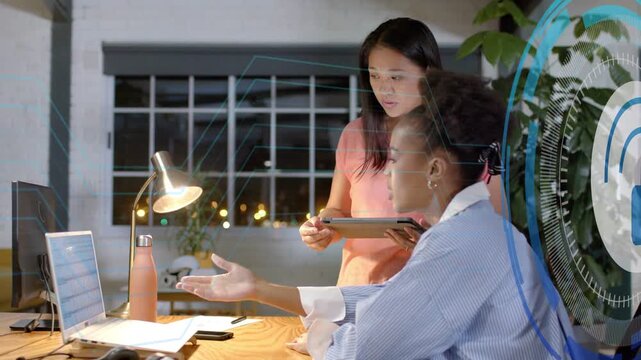 Seated woman pointing to laptop causing lock UI rising while peer holding tablet checking security