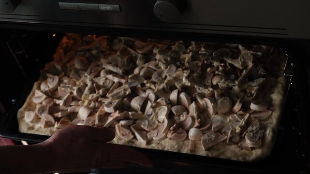 Chef putting a baking sheet with raw mushroom pizza into a hot oven to bake.
Close-up of the process of cooking a homemade champignon pie in the kitchen.