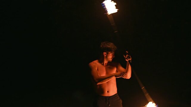 Young hispanic man performing fire twirling at night
