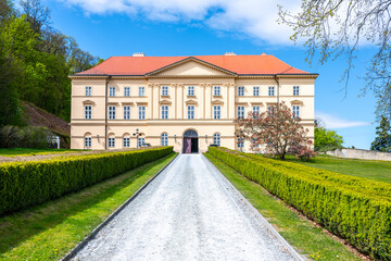 Boskovice Castle stands tall in Czechia under a bright blue sky. Visitors can see the castle's impressive facade and well-kept gardens as they walk along the gravel path leading to the entrance. © pyty