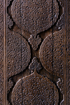 Ornate carved wooden door detail from Muhammad Amin Khan Madrasah in Khiva. Intricate floral arabesque medallions on dark wood - traditional Central Asian craftsmanship. Carved wood texture, pattern.