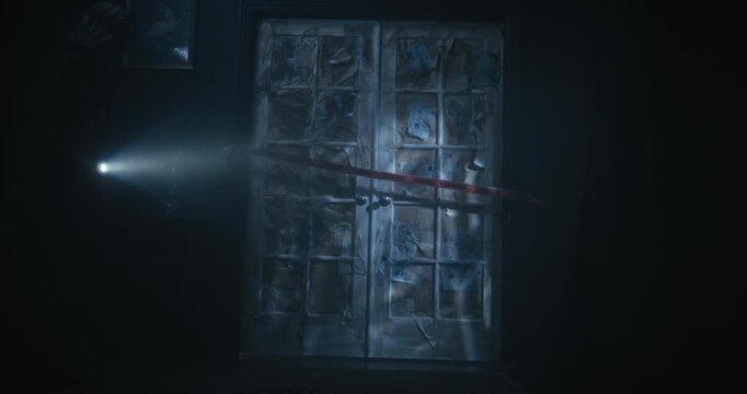 Cautious, alone woman with flashlight pulling evidence tape off creepy door and entering scary, dark room - dolly in shot